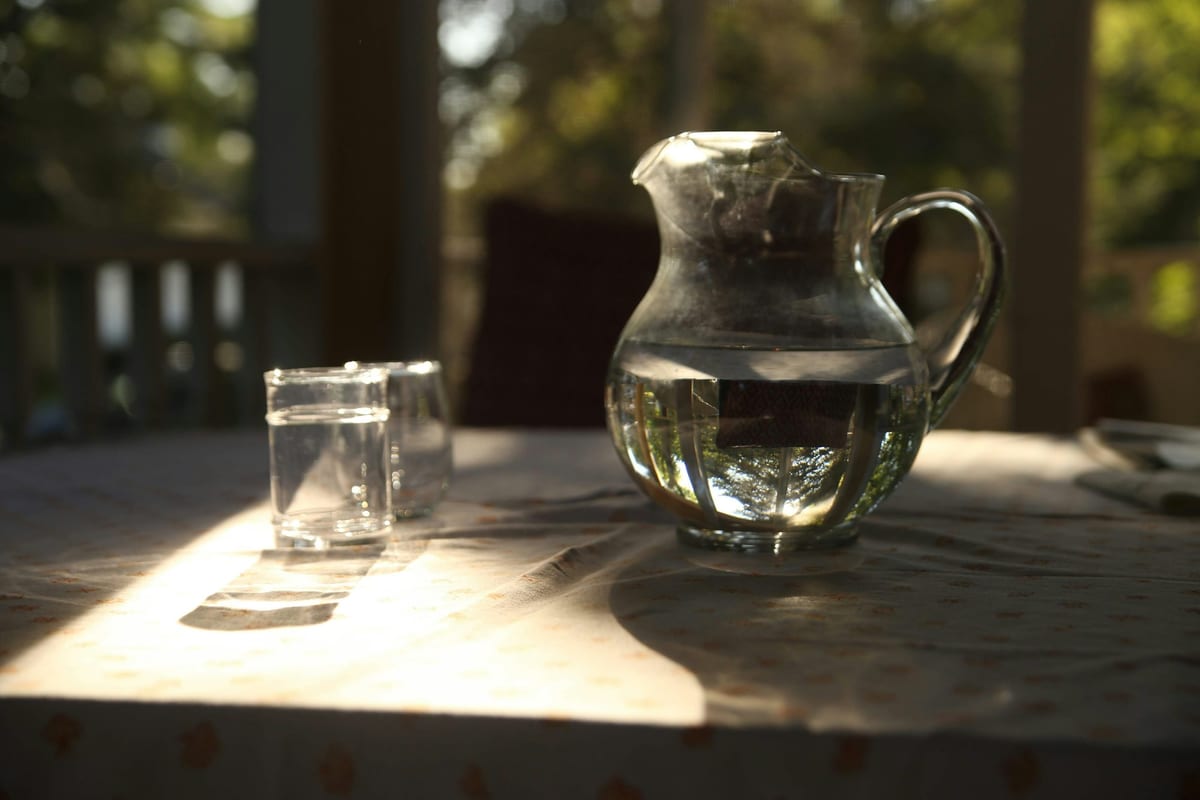 A glass and a pitcher of water on a table by a window in soft morning light