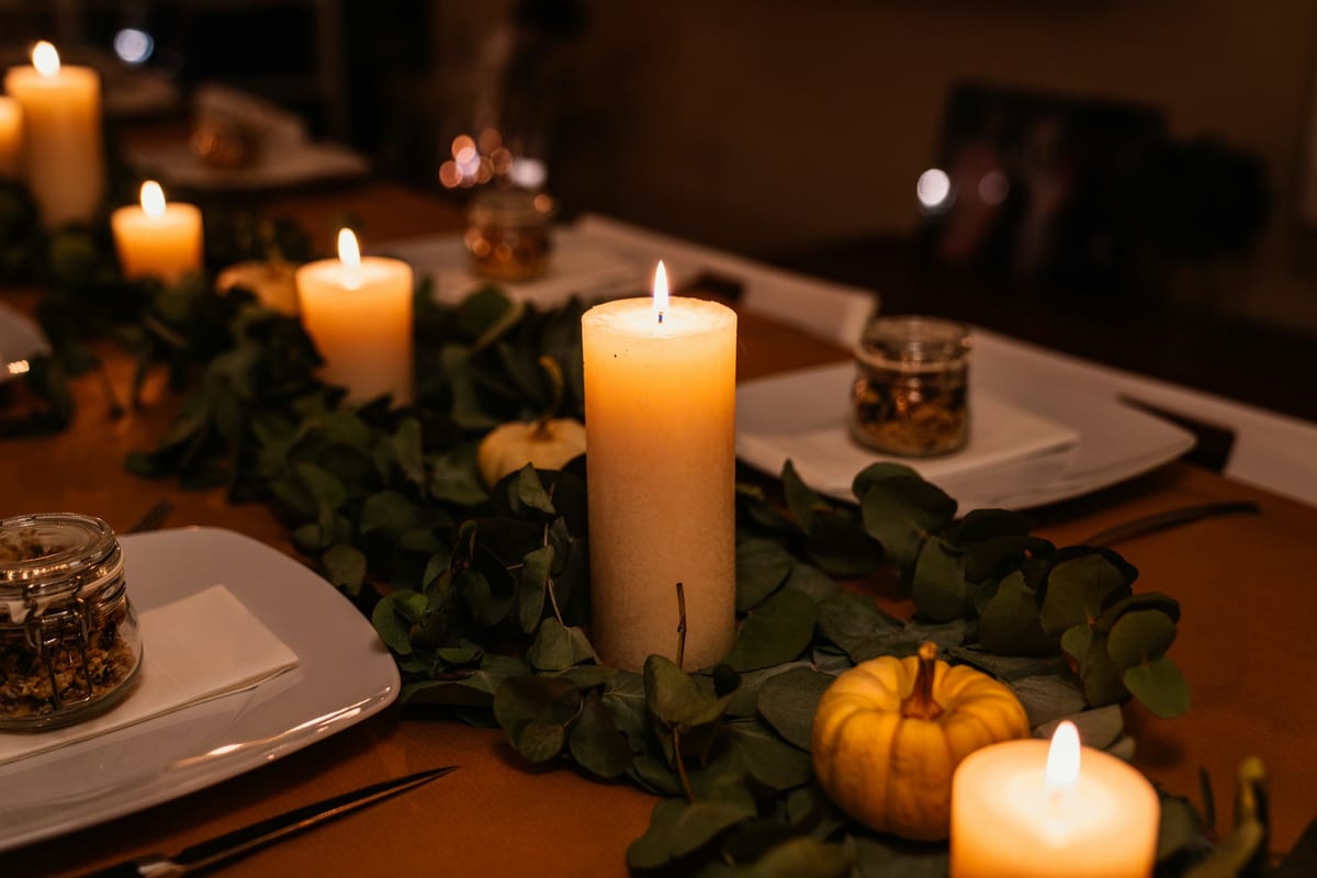 Lit pillar candles, greenery and small pumpkins on a dinner table at night